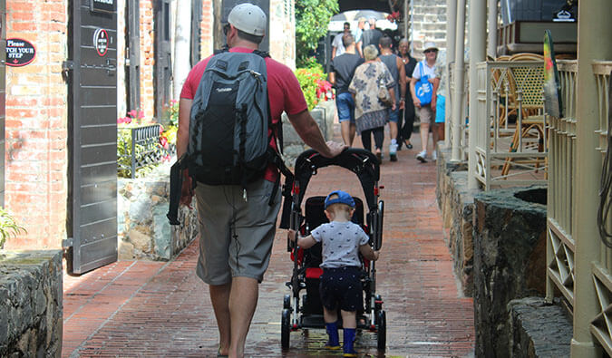 a father pushing a buggie down a street with a toddler stood on the back on the buggie