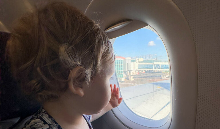 A young baby looking out a small airplane window