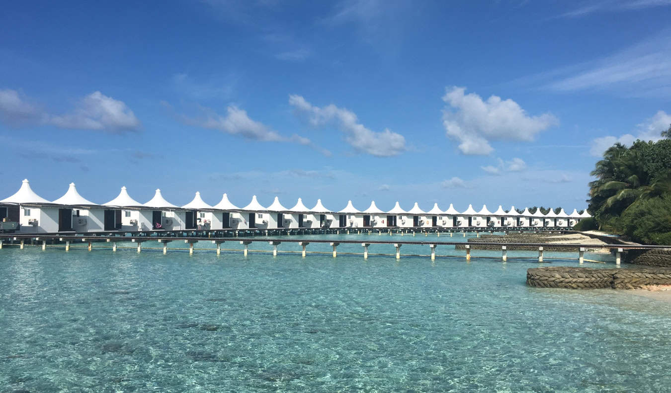 A row of white bungalows over the stunningly clear blue waters of the Maldives