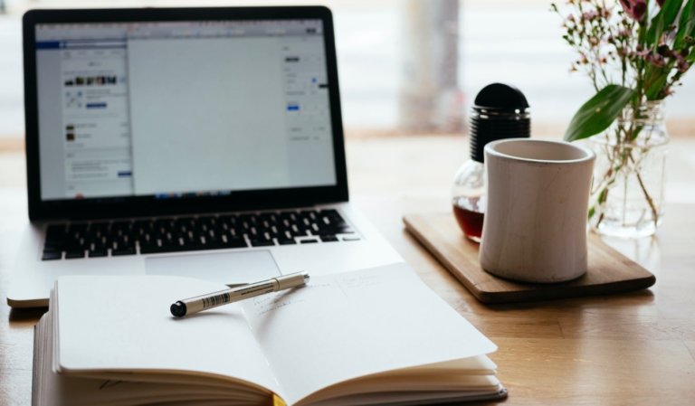 A laptop on a table with a notebook and a coffee