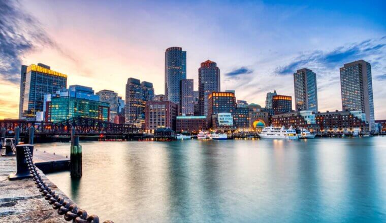 The towering skyline of Boston, MA as seen from near the water with a blue sky above