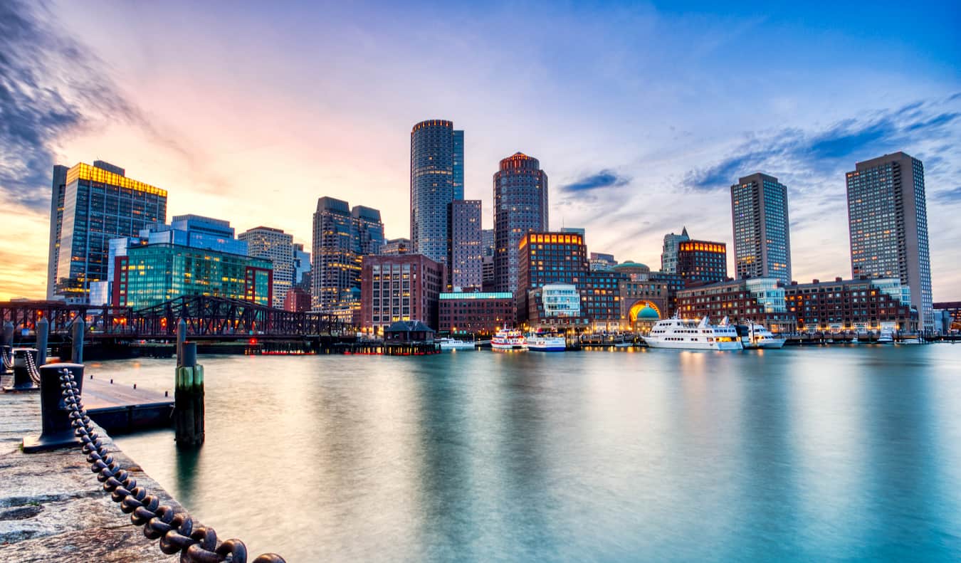 The towering skyline of Boston, MA as seen from near the water with a blue sky above