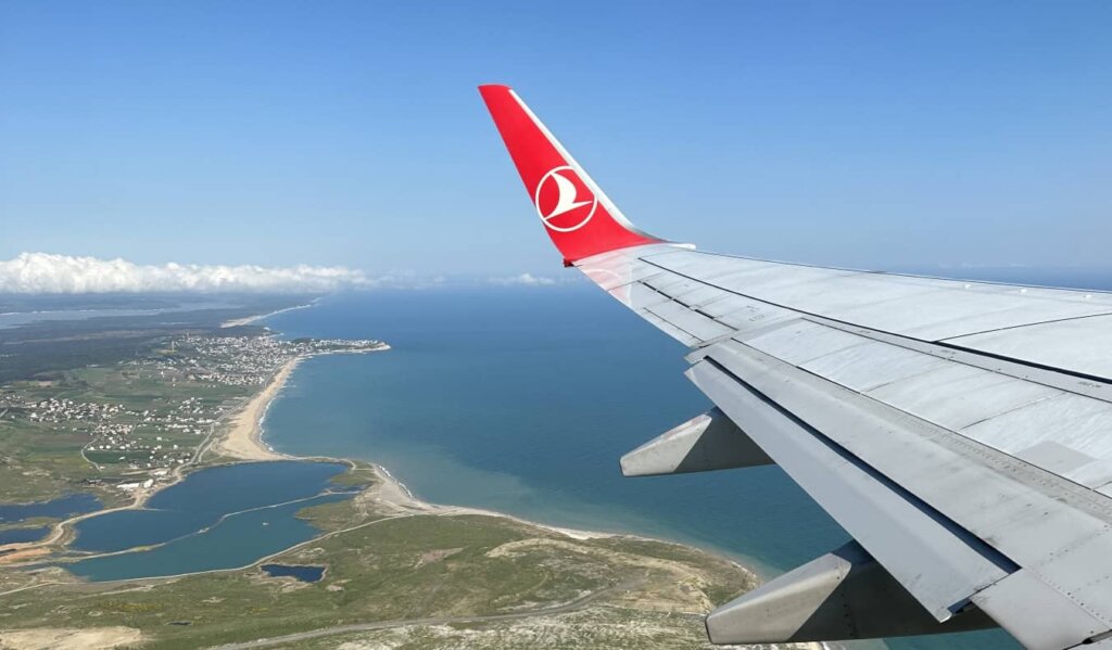 The wing of a plane with the Turkish airlines logo, flying high over a shoreline