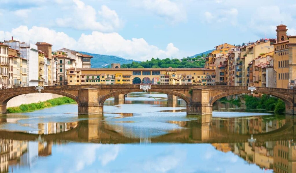 Panoramic of Ponte Vecchio stretching across the Arno River in Florence Italy, with both banks of the river as well as the bridge lined with yellow buildings