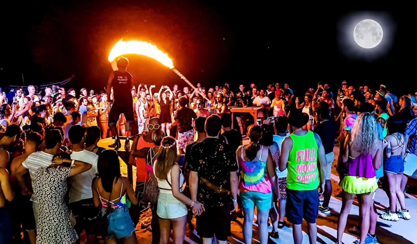 A crowd of people watch flame dancers and throwers at the Full Moon Party on a beach in Thailand