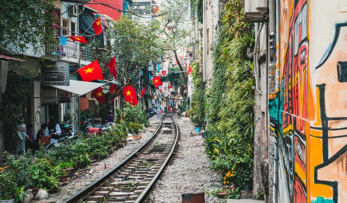 Train tracks running between close-together buildings in bustling Hanoi, Vietnam”/></noscript><br/>
<a href=