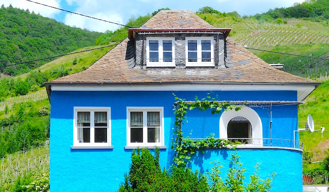 A bright blue villa surrounded by vineyards with lush greenery in the background