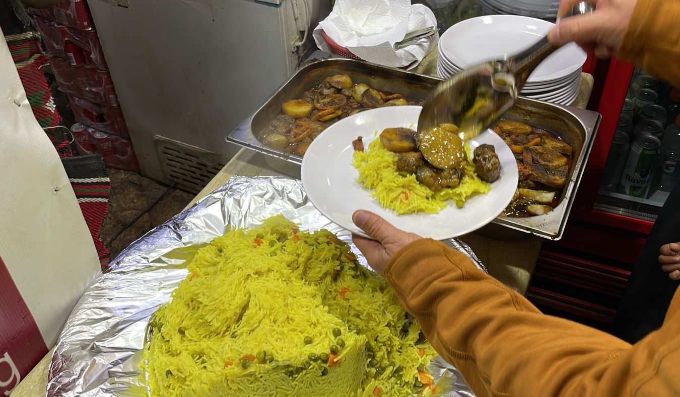 A person dishing out a plate of homecooked yellow rice and stew in Aman, Jordan