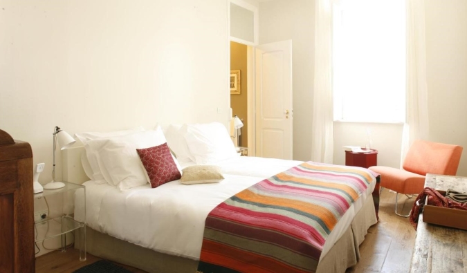 A simple guest room with wide-planked wooden floors, a white bed with a colorful blanket, and large windows letting in a lot of light at A Casa das Janelas com Vista, a bed and breakfast in Lisbon, Portugal