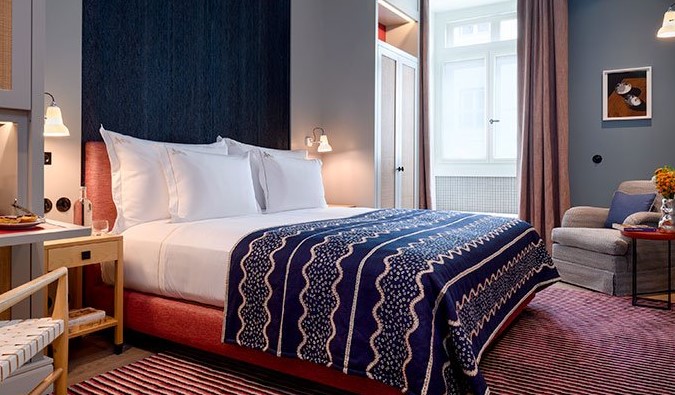 A guest room with blue walls, a magenta rug and curtains, and a king-sized bed with a patterned blanket at Bairro Alto Hotel in Lisbon, Portugal