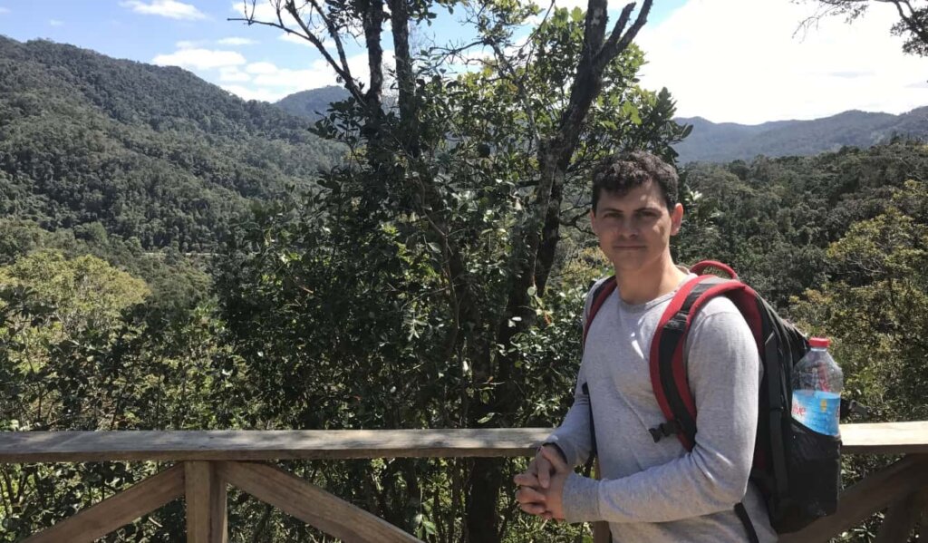 Nomadic Matt with a backpack on standing in front of forested mountains