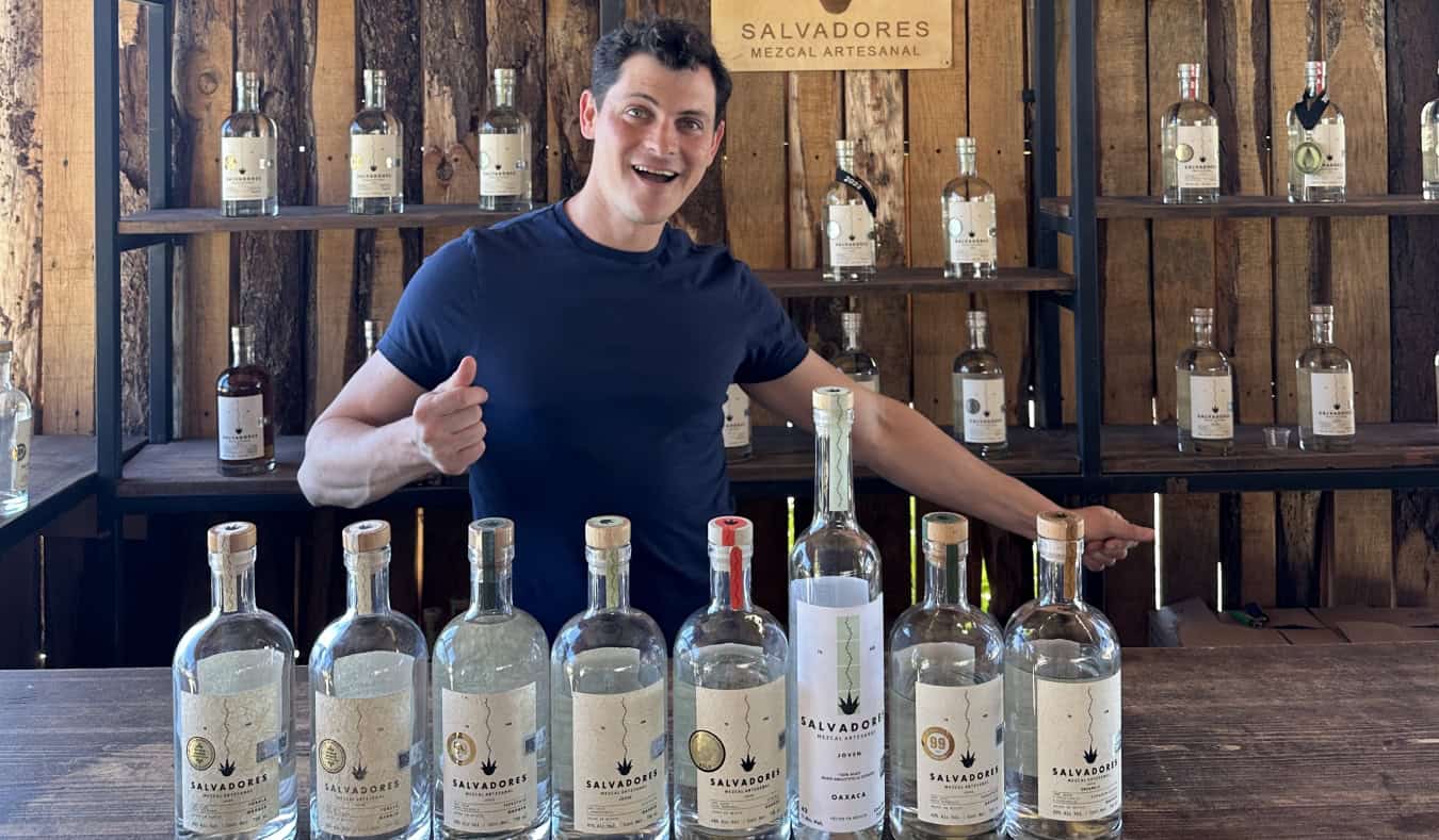 Nomadic Matt standing in front of a row of mezcal bottles in Oaxaca, Mexico