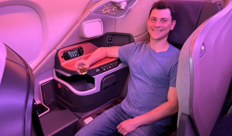 Travel blogger Nomadic Matt holding a glass of wine while sitting on an airplane in first class