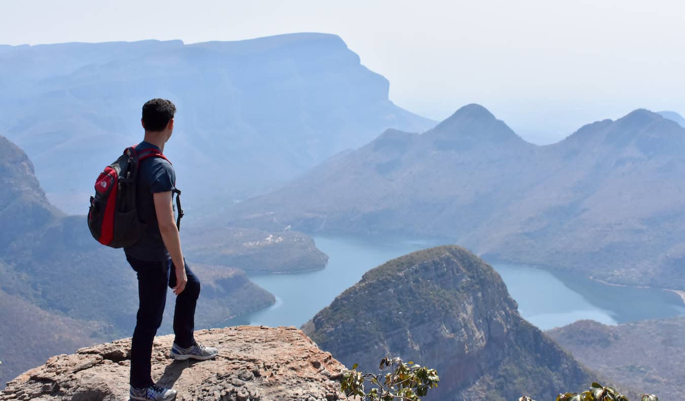 Nomadic Matt posing on the ridge of a towering canyon in South Africa with mountains in the distance