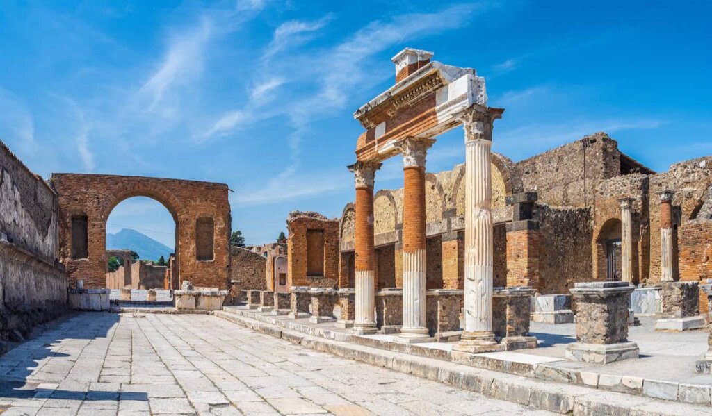 Cobblestone street in Pompeii lined with ruins of buildings on a bright and sunny day in Italy