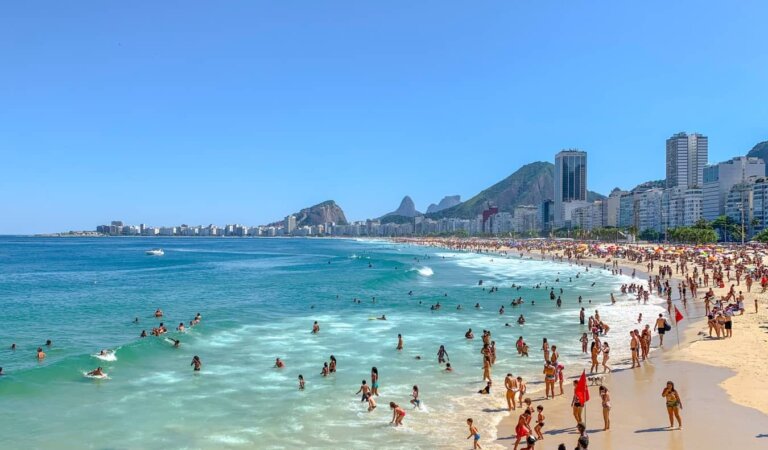 People having fun in the ocean along a long stretch of beach lined with multistory buildings in Rio de Janeiro, Brazil