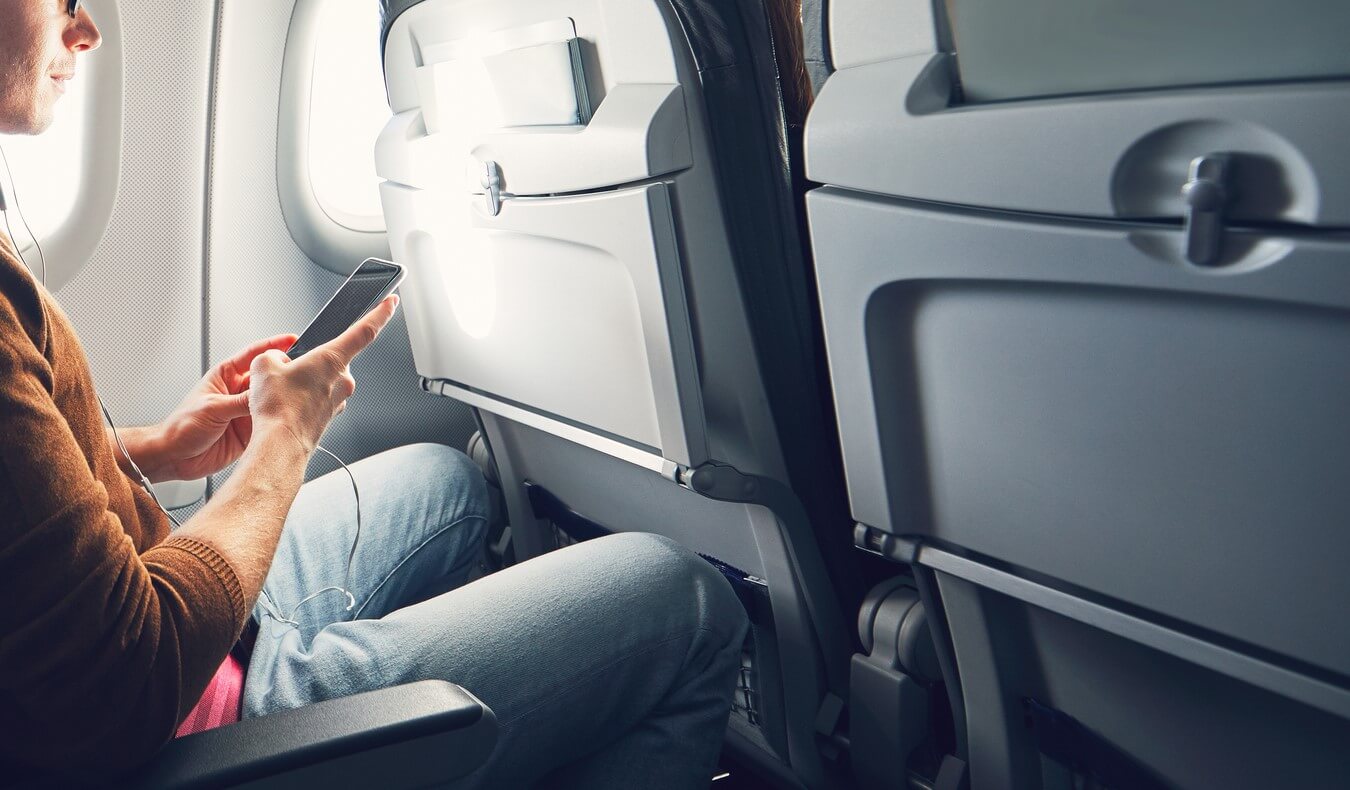 A man sitting on an airplane holding a smartphone in his hands