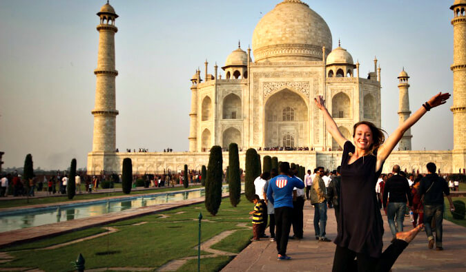 woman jumping with arms raised to the right of the Taj Mahal