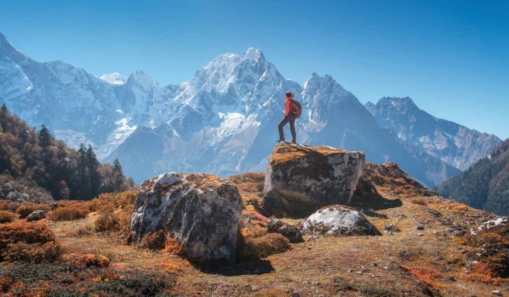 woman standing on a rock with jagged snow capped mountains in the background