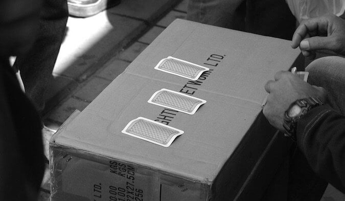 A cardboard box with 3 playing cards on it outside on a street