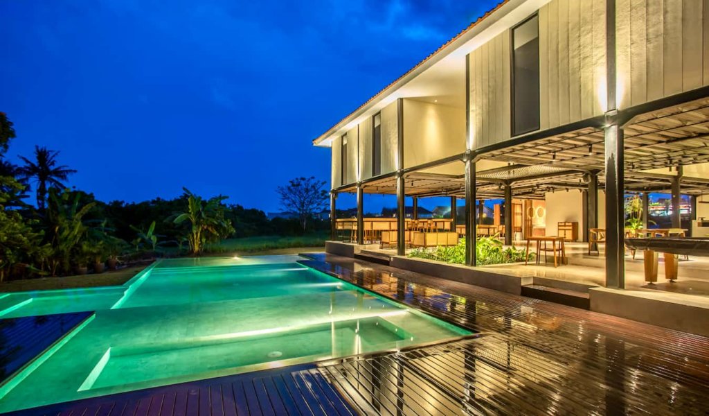 The exterior of the Tribal Bali hostel at night with the pool lit up in the foreground