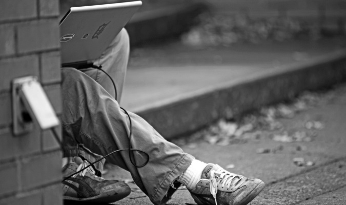 Traveler plugging laptop into a public outlet outside while using free Wi-Fi