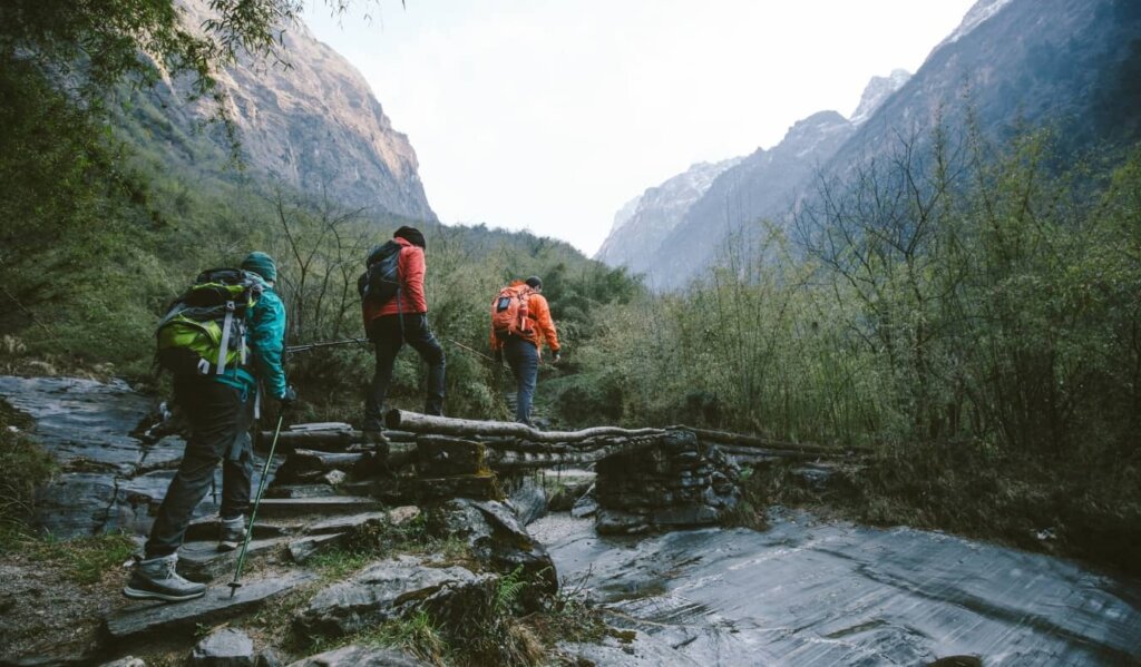 Group of trekkers cross a wooden bridge heading towards mountains in the Annapurna region of the Himalayas